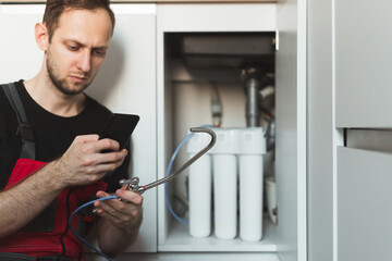 Plumber in the kitchen with smartphone read guide how to install household water treatment system....