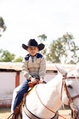 A child ridding a horse in cowboy outfit in a ranch