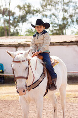 A boy ridding a horse in cowboy clothes in a farm