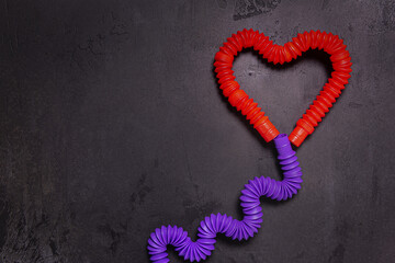 Tube toys bent as red heart balloon and wavy ribbon on black concrete