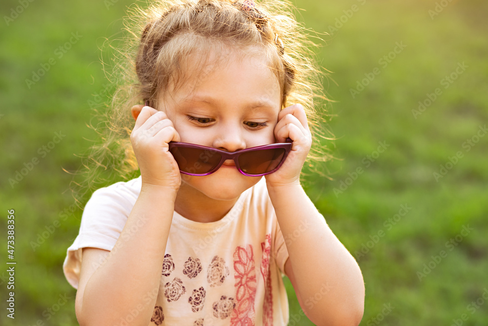 Wall mural Fun kid girl in sunglasses on green glass outdoor summer background. Closeup