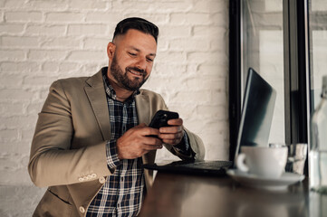 Businessman using smartphone and a laptop while drinking coffee in a cafe