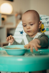 Adorable little baby eating his dinner and making a mess