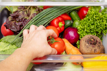 Mans hand is opening drawer of refrigerator with vegetables. Healthy and right food