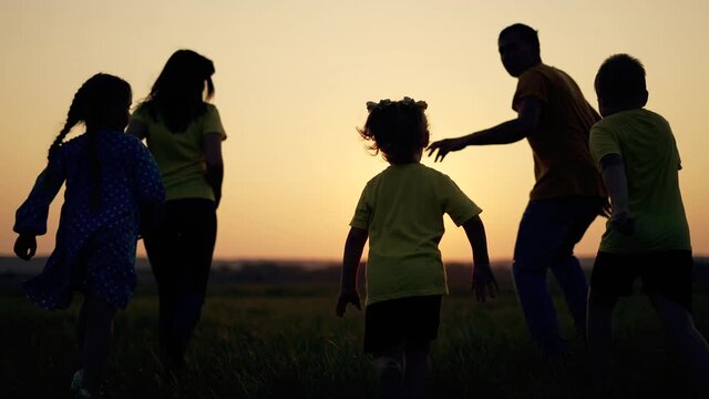 Happy family at sunset.Group of children and parents in field on green grass.Family run on grass in park.Summer people silhouette. Family vacation together in nature. Dad mom and children run in field