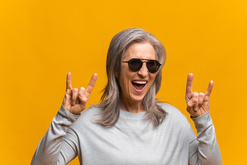 Crazy positive sanguine senior woman in sunglasses is showing sign of horns, funny hilarious mature...