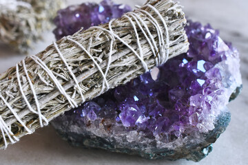 A close up image of a white sage smudge stick on a deep purple amethyst cluster geode.  