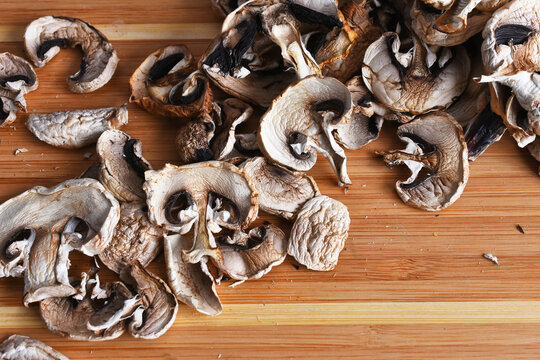 A top view image of dehydrated organic white and brown mushrooms on a wooden cutting board. 