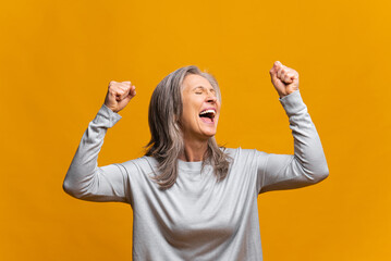 Overjoyed excited modern mature woman celebrating goal achievement, raising fists isolated on...