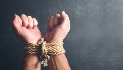 Male hands tied with a rough rope at the wrists close-up on a dark background, soft focus....