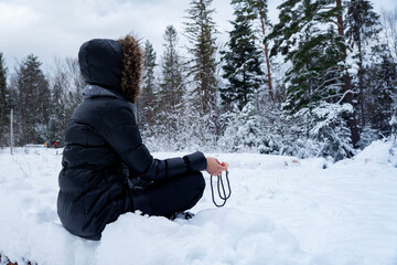 Fototapeta na wymiar A young woman meditates in the lotus position on the wooden log covered with snow. Yoga lotus position, asana meditation in the forest, mindfulness, zen. 