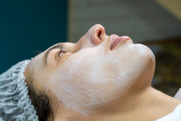 Beauty clinic concept. Young woman getting professional facial procedure. Beautician spreads  mask on female face with brush. Face renovation concept. 