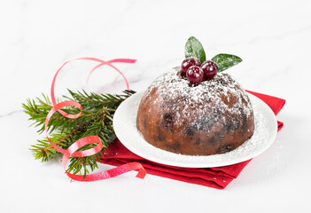 Christmas English pudding with dried fruits, almonds, honey, rum, decorated with powdered sugar and cranberries on a plate on a red napkin on a white background