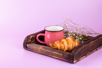 Wooden tray with croissant, coffee cup and white flowers on pink background