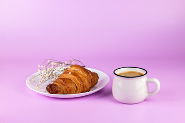 Cup of coffee and croissant on the white plate with flower branch on pink background. Morning romantic breakfast concept.