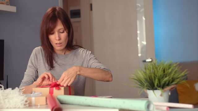 Woman cutting wrapping paper wrapping gift box by festive ribbon at home