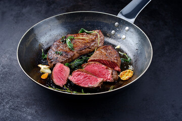 Traditionell gebratene Rumpsteaks vom Bison Rind mit Kräutern und Knoblauch serviert in einer rustikalen Bratpfanne als close-up