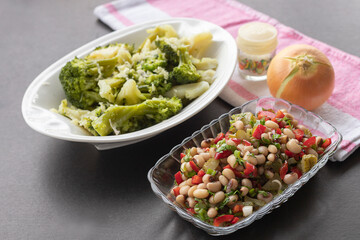 In the background broccoli salad in front Red pepper, pickled cucumbers, fresh onions Dried cowpea salad