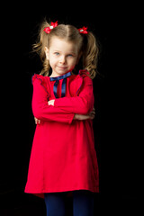 Cute blonde little girl standing on black backdrop