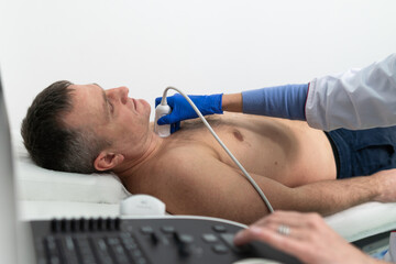 Doctor using ultrasound machine to scan heart of a male patient. Cardiologist makes a patient an...