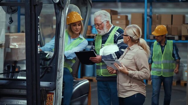 Elderly male warehouse supervisor instructing to a female worker sitting in a forklift
