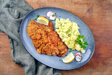 Traditional deep-fried schnitzel with potato salad and lemon slices served as top view on a modern Nordic design plate with copy space