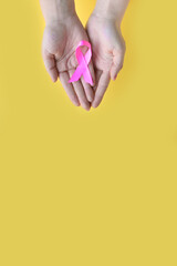 Breast Cancer Awareness. Concept I Am and I Will. Hands of woman holding pink ribbon on yellow background. World cancer day