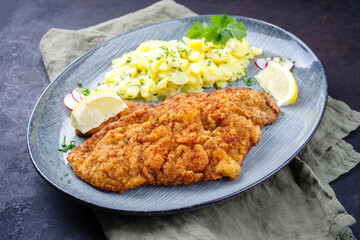 Traditionelles frittiertes Schnitzel mit Kartoffelsalat und Zitronenscheiben serviert als close-up auf einem Design Teller 