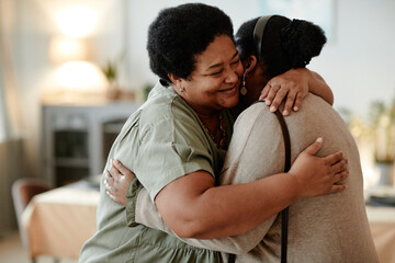 Portrait of senior African-American woman embracing daughter and smiling while welcoming guests for...