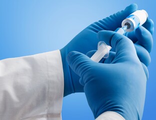 Glass bottle with injection shot, hand in blue gloves holding syringe with needle
