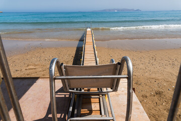 Fototapeta na wymiar Safe motorized wheelchair ramp, used to transport disabled people into the sea water for swimming. Heraklion, Crete, Greece