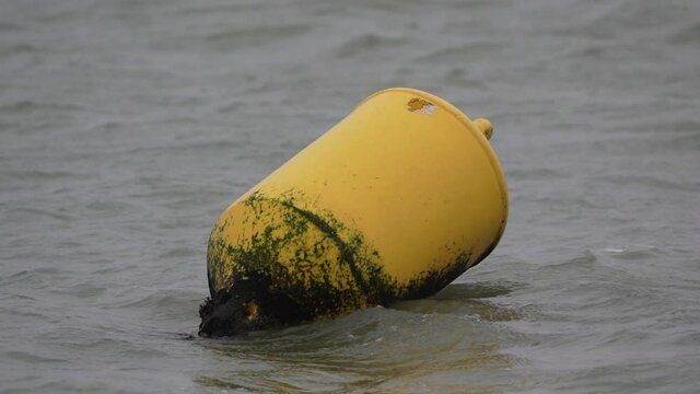 A yellow buoy is bobbing on the waves in a strong wind