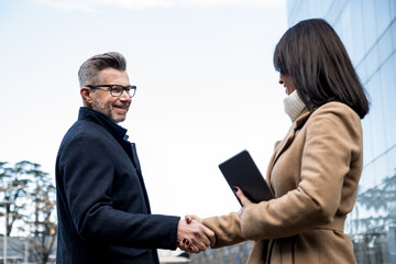 Business man shaking hands with partner in front of office buildings in the city - greeting,...
