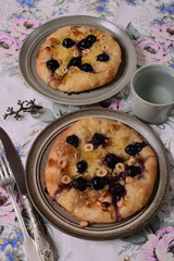 Homemade mini pizza with cheese, nuts and black grapes on plates.