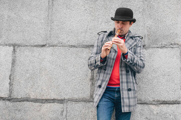 Street lifestyle. Street musician playing a wooden instrument sopilka on the background of a gray wall