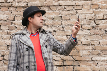 Portrait of a man with a phone in his hands on the background of a brick wall outdoors.