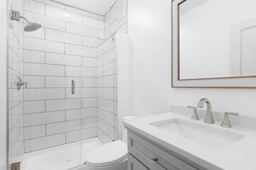 A white bathroom with a grey vanity cabinet, white marble countertop, and a shower with large...