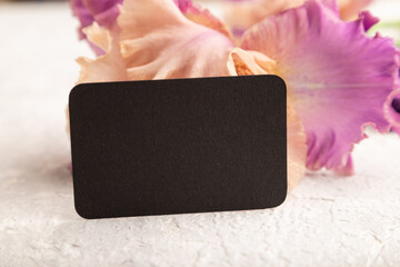 Black business card with iris purple flowers on white concrete background. side view, copy space.