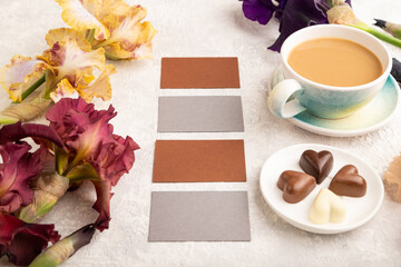 Set of gray and brown business cards with cup of cioffee, chocolate candies, iris flowers on gray concrete background. side view, copy space.