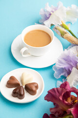 Cup of cioffee with chocolate candies, lilac and purple iris flowers on blue pastel background. side view, copy space.