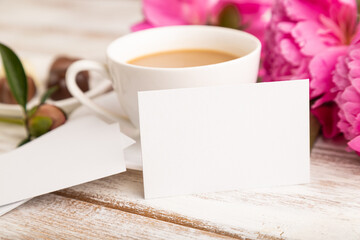 Fototapeta na wymiar White business card with pink peony flowers and cup of coffee on white wooden background. side view, copy space.