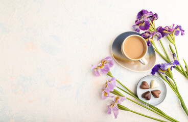Obraz na płótnie Canvas Cup of cioffee with chocolate candies and lilac iris flowers on white concrete background. top view, copy space.