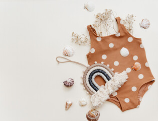 Cute swimsuit for baby on beige background with seashells, minimal summer kids concept. Top view,...