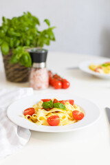 Italian pasta with cherry tomatoes, tomato sauce and cheese, garnished with a sprig of basil. Ready lunch or dinner. Table setting