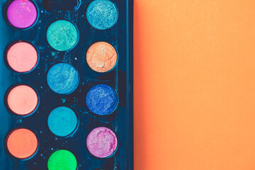 Colorful watercolours for childern in a plastic, black box against orange background.