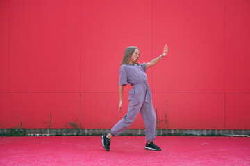 Fototapeta na wymiar Active teen girl dancing outdoors on red wall background. Stylish modern young dancer perform contemporary hip hop dance