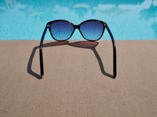 Close up of sunglasses laying besides pool. Summer time background, holidays, travel concept.