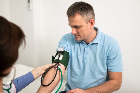 Medical and healthcare concept. Hypertension, high blood pressure and stroke precursors in middle age in men. Medical checkup. Female doctor in general practice measures pressure to patient in clinic.