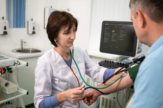 Medical and healthcare concept. Hypertension, high blood pressure and stroke precursors in middle age in men. Medical checkup. Female doctor in general practice measures pressure to patient in clinic.