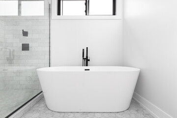 A renovated, standalone tub with a black faucet, small hexagon tiles on the floor, and a shower with glass walls and large marble subway tiles.
